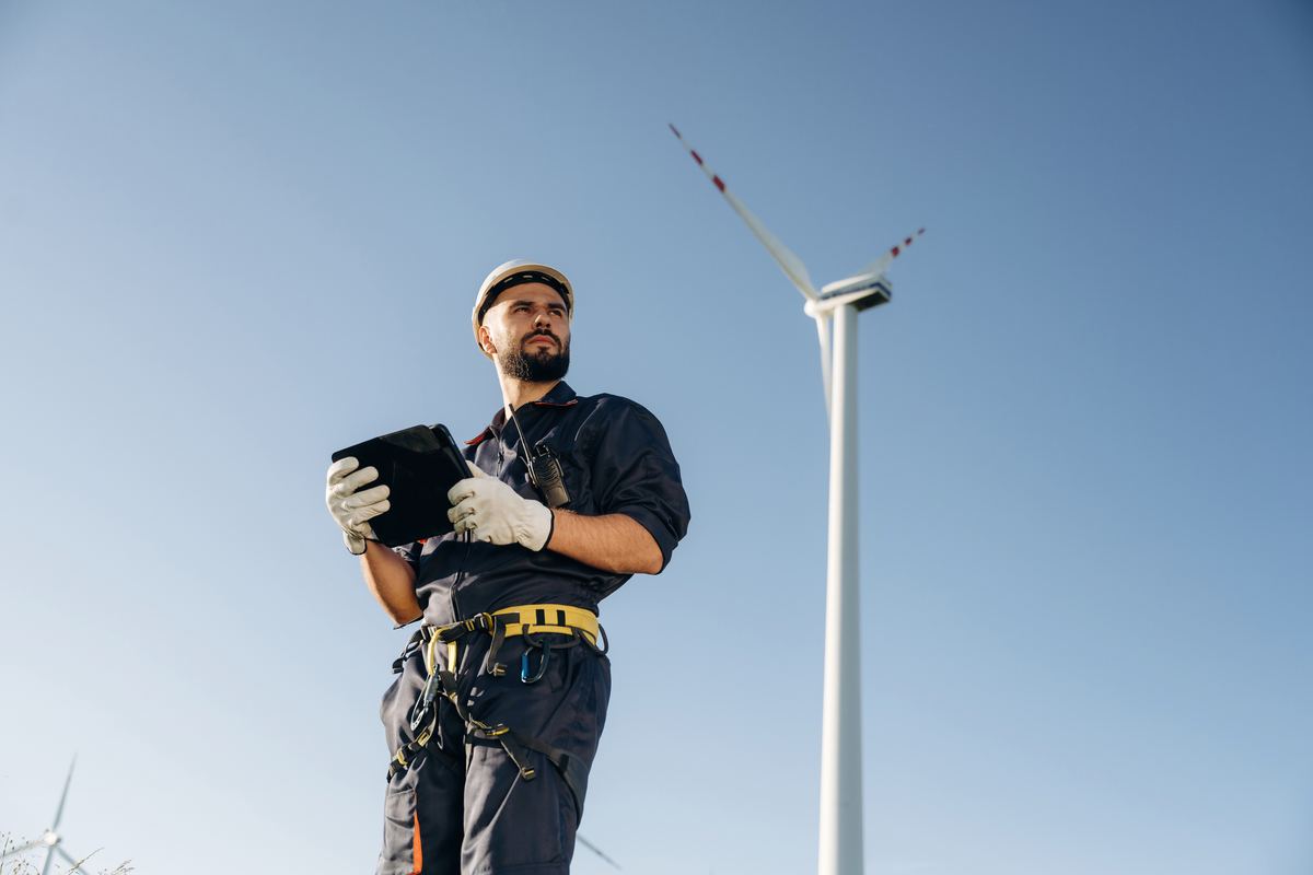 An engineer checking readings on a tablet beside a wind turbine