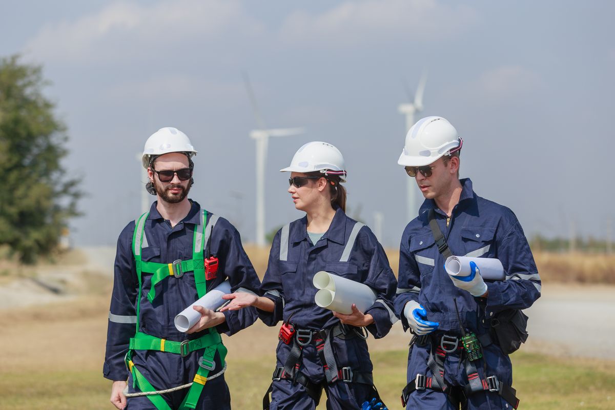 Three wind turbine technicians in harnesses being briefed at a wind farm