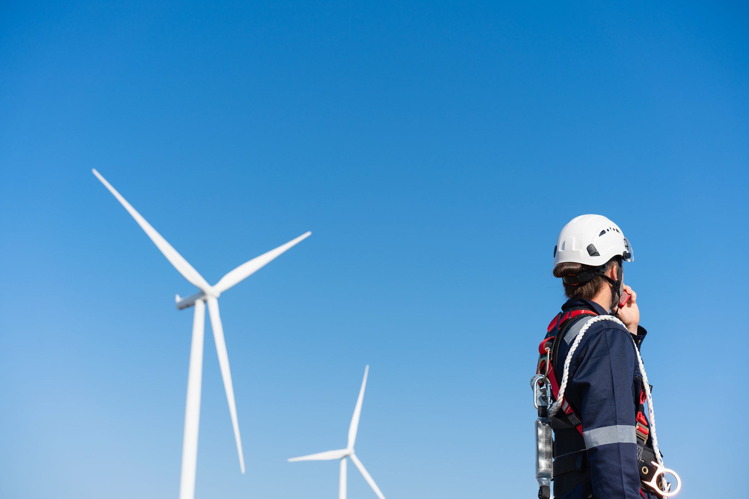 A wind turbine technician in a harness looking up at a turbine
