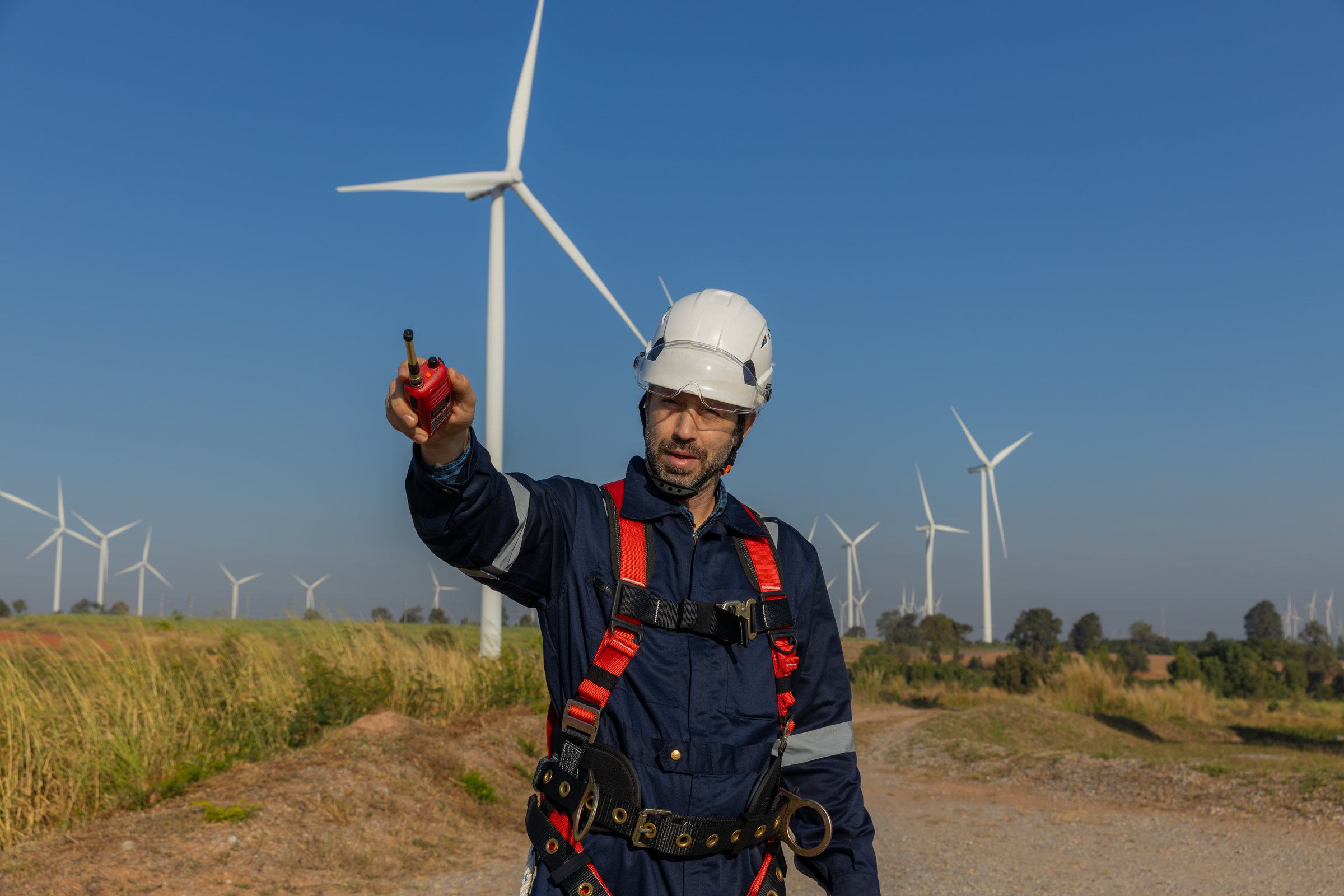 A wind farm engineer in high-visibility PPE using a radio on site