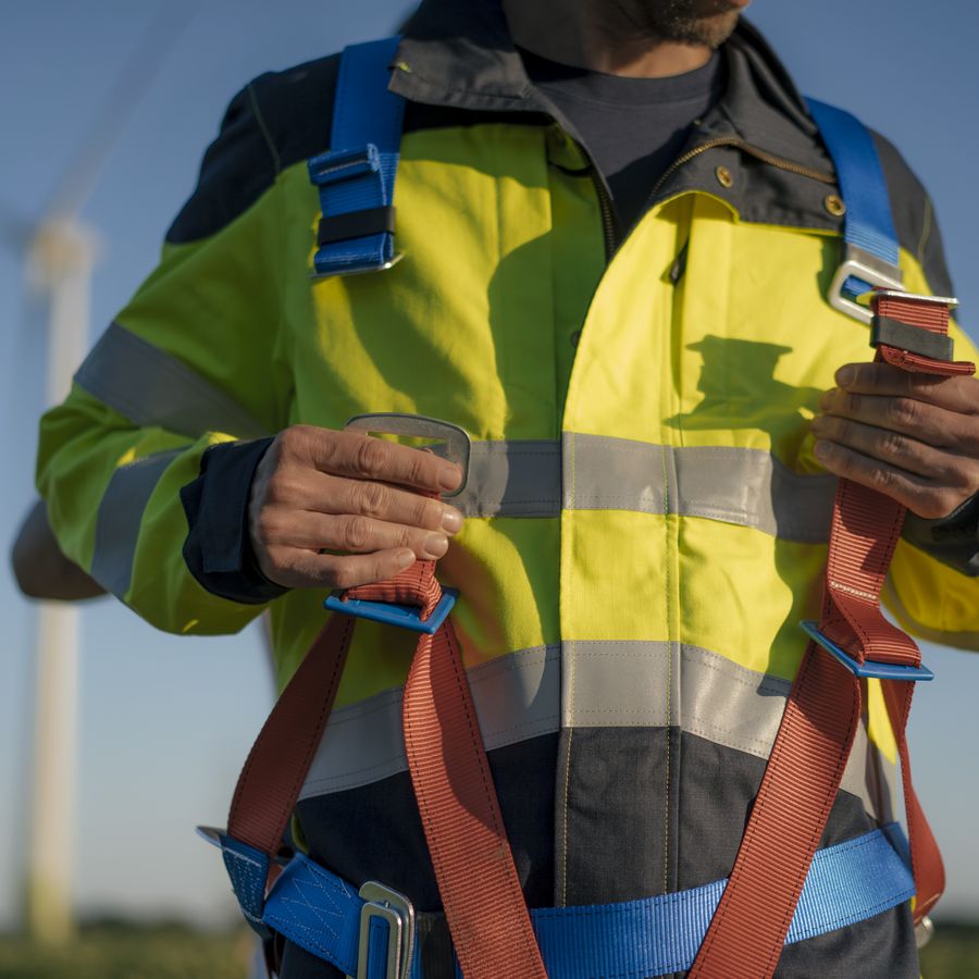A wind turbine technician fastening a fall-arrest harness before climbing