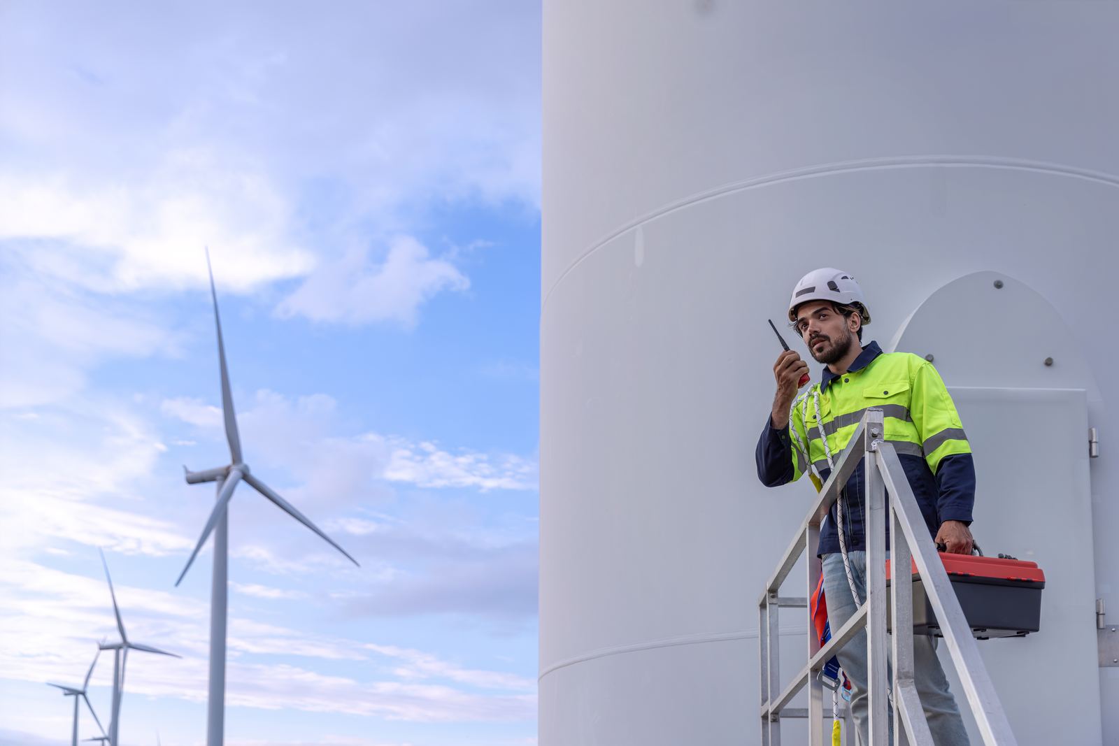 A technician working at height on a wind turbine with a wind farm behind
