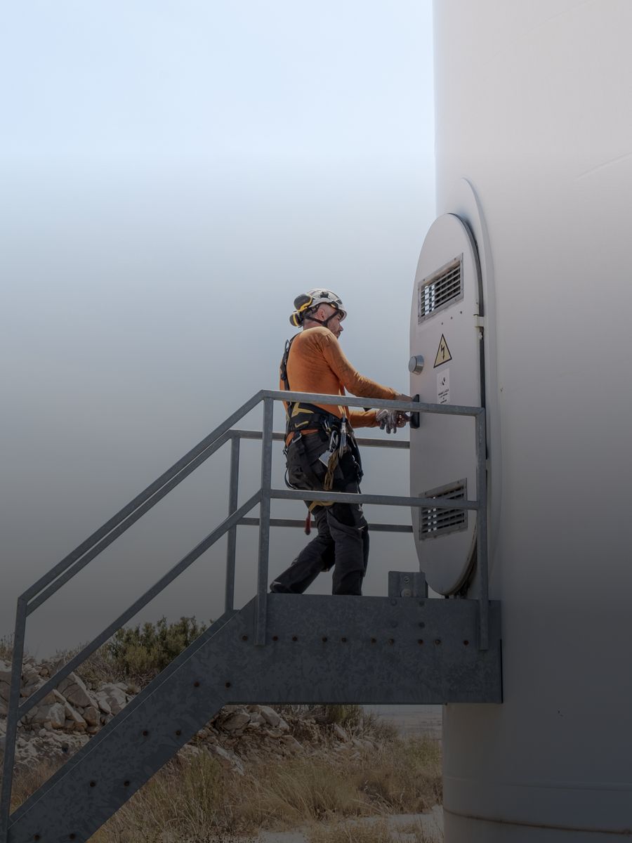 A technician in a harness at the base of a wind turbine tower